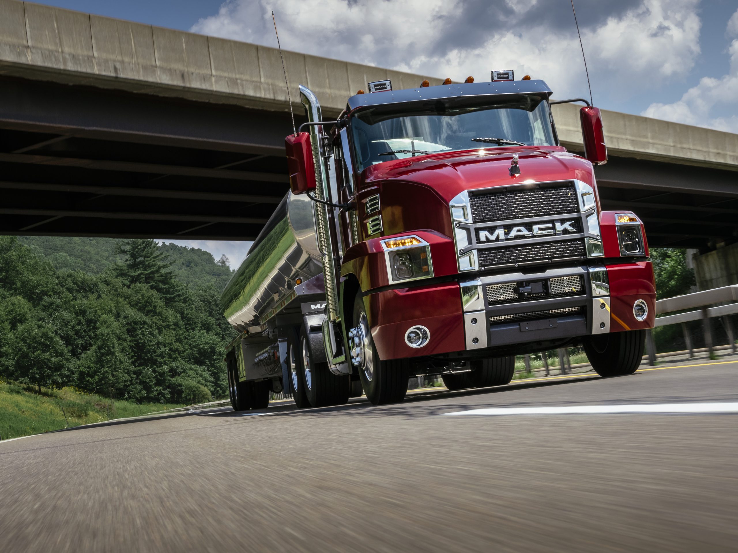 red mack truck on the road driving underneath a bridge